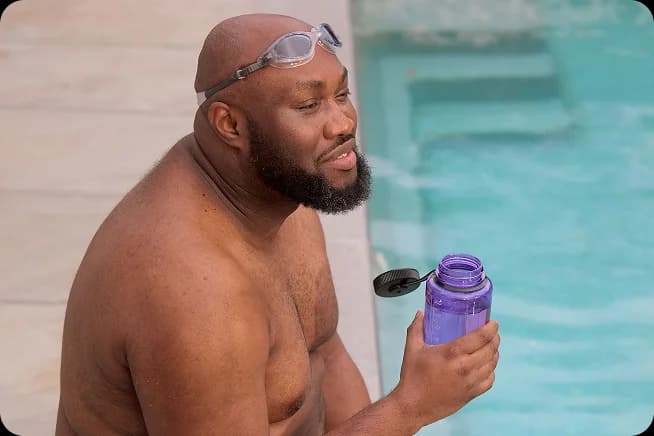 A man with swimming goggles holding a water bottle by a pool