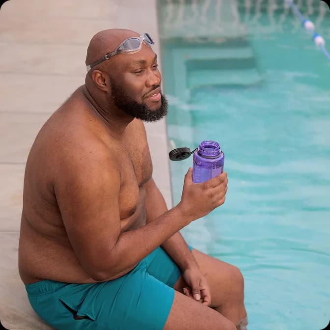 A man with swimming goggles holding a water bottle by a pool