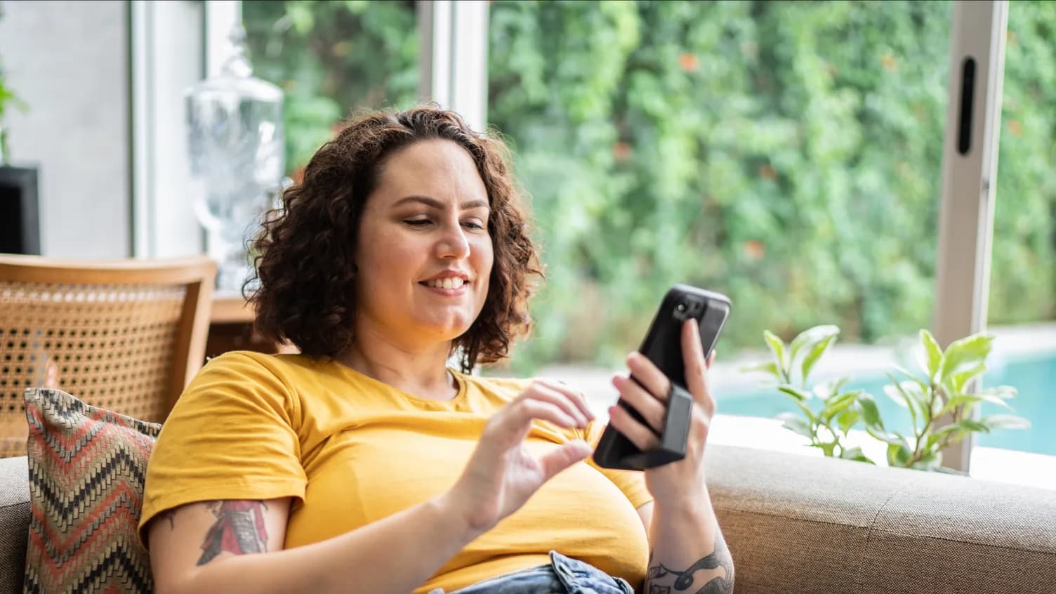 A customer smiling while checking their phone on a sofa