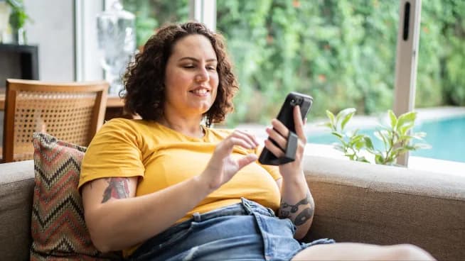 A customer smiling while checking their phone on a sofa