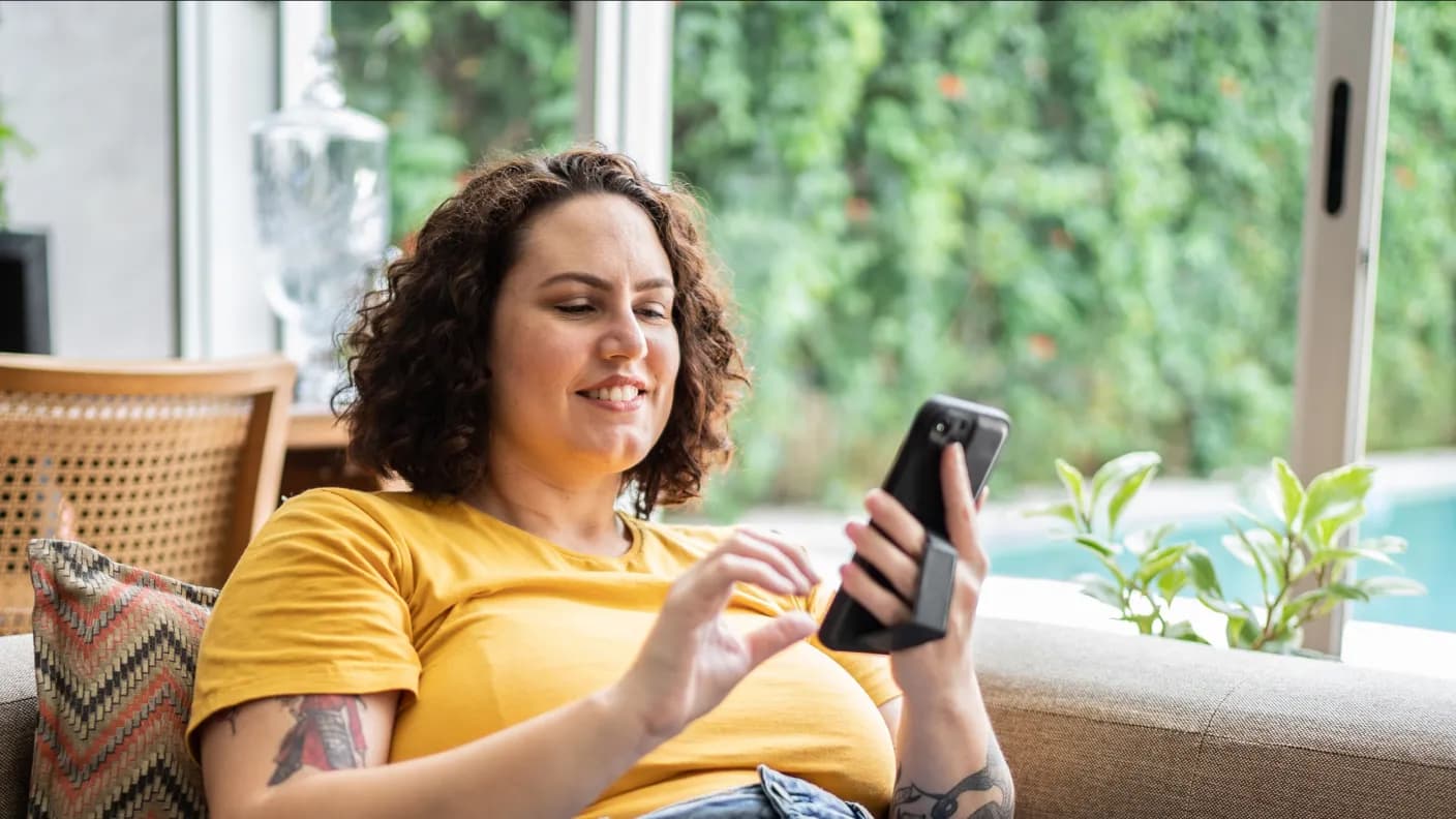 A customer smiling while checking their phone on a sofa