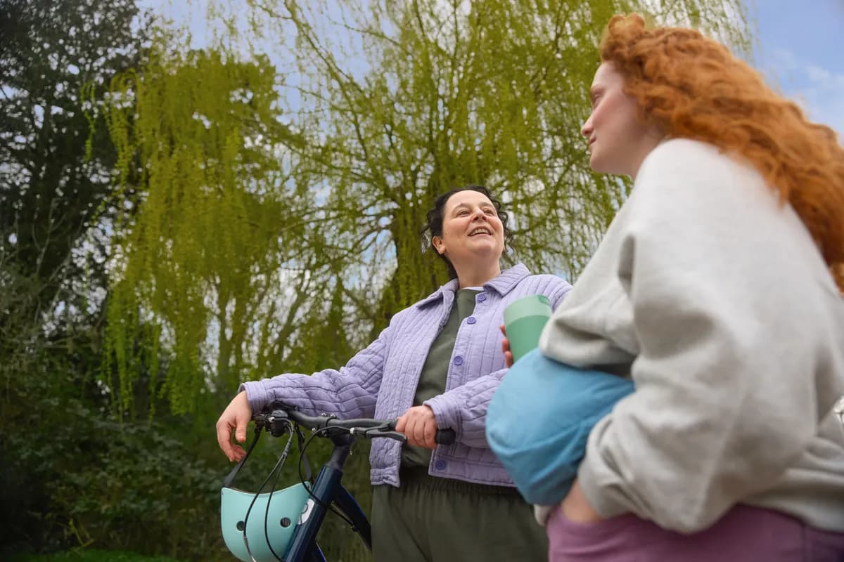 Two women laughing together outdoors, with trees in the background.